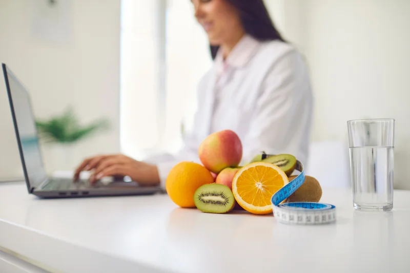 Ernährungsberaterin am Laptop, daneben frisches Obst und ein Maßband – Terminfindung kostet Zeit