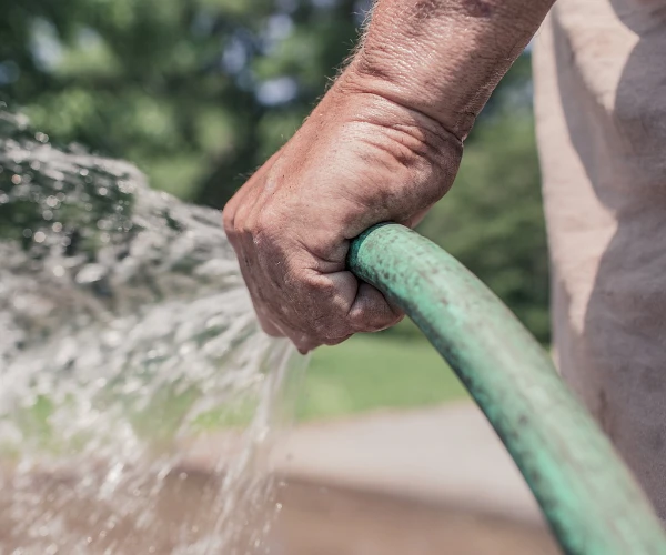 Hand hält Wasserschlauch mit laufendem Wasser