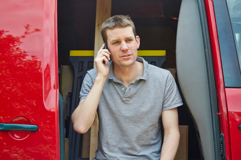 Handwerker telefoniert am Transporter vor dem Einsatz – Terminabsprachen kosten Arbeitszeit