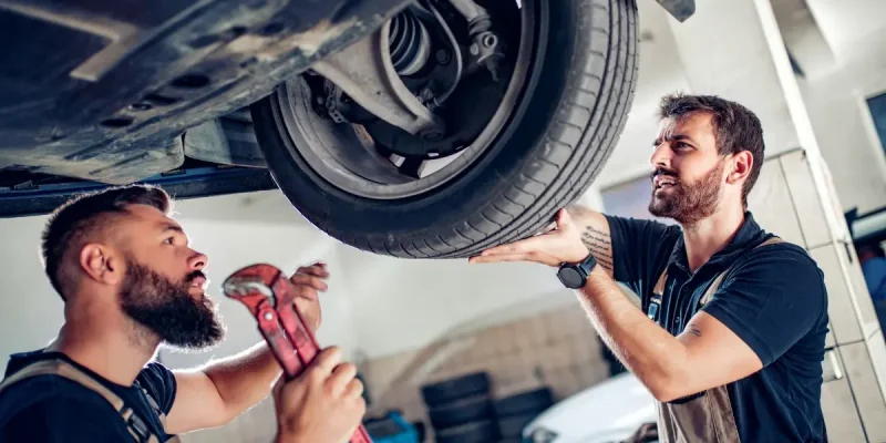 Zwei Mechaniker arbeiten an der Hebebühne – Verwaltung frisst Zeit, die für Fahrzeuge fehlt