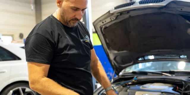 KFZ-Meister am geöffneten Motorraum in der Werkstatt – Terminabsprachen kosten Arbeitszeit