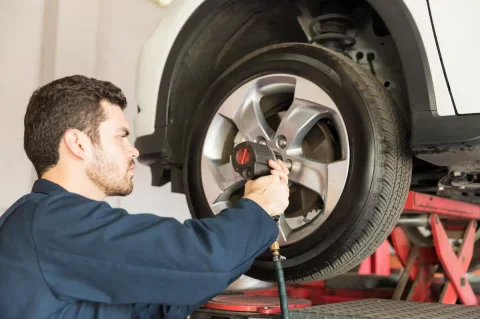 Mechaniker in blauer Arbeitskleidung löst mit einem Druckluftschrauber die Radschrauben an einem Auto auf der Hebebühne