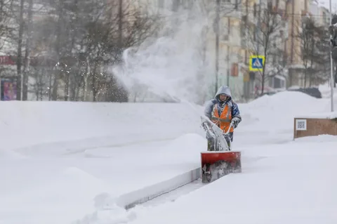 Mitarbeiter eines Winterdienstes räumt mit der Schneefräse einen Gehweg frei