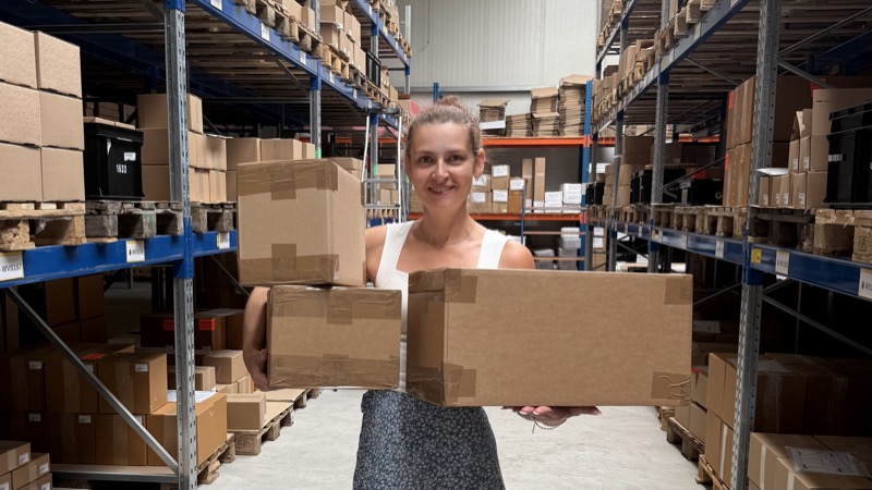 Lächelnde Mitarbeiterin im modernen Fulfillment-Lager von WVS-Versand mit Paketen - professionelle E-Commerce Logistik und Versandabwicklung