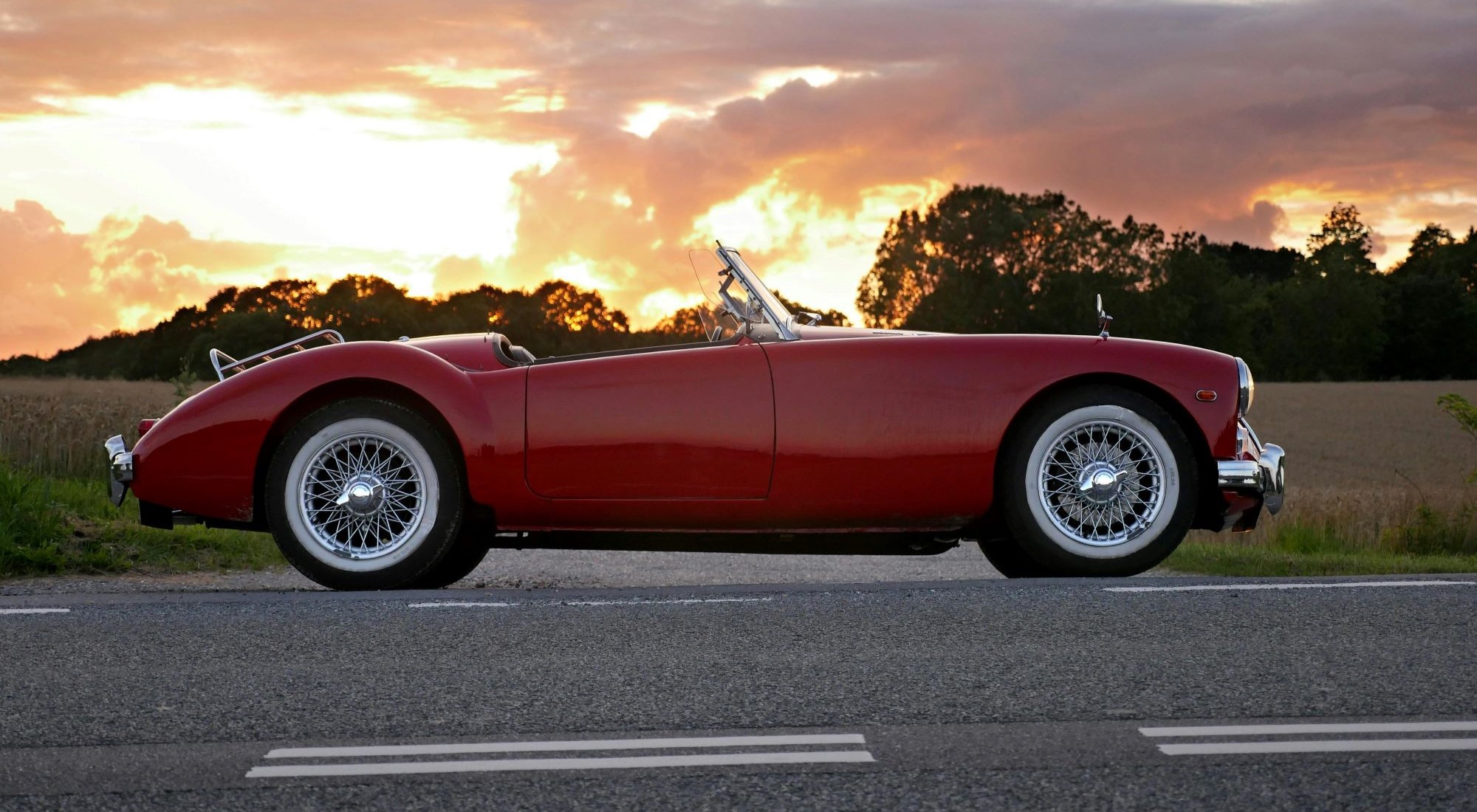 ein Bild, das ein rotes Cabriolet auf der Straße im Sonnenuntergsng zeigt