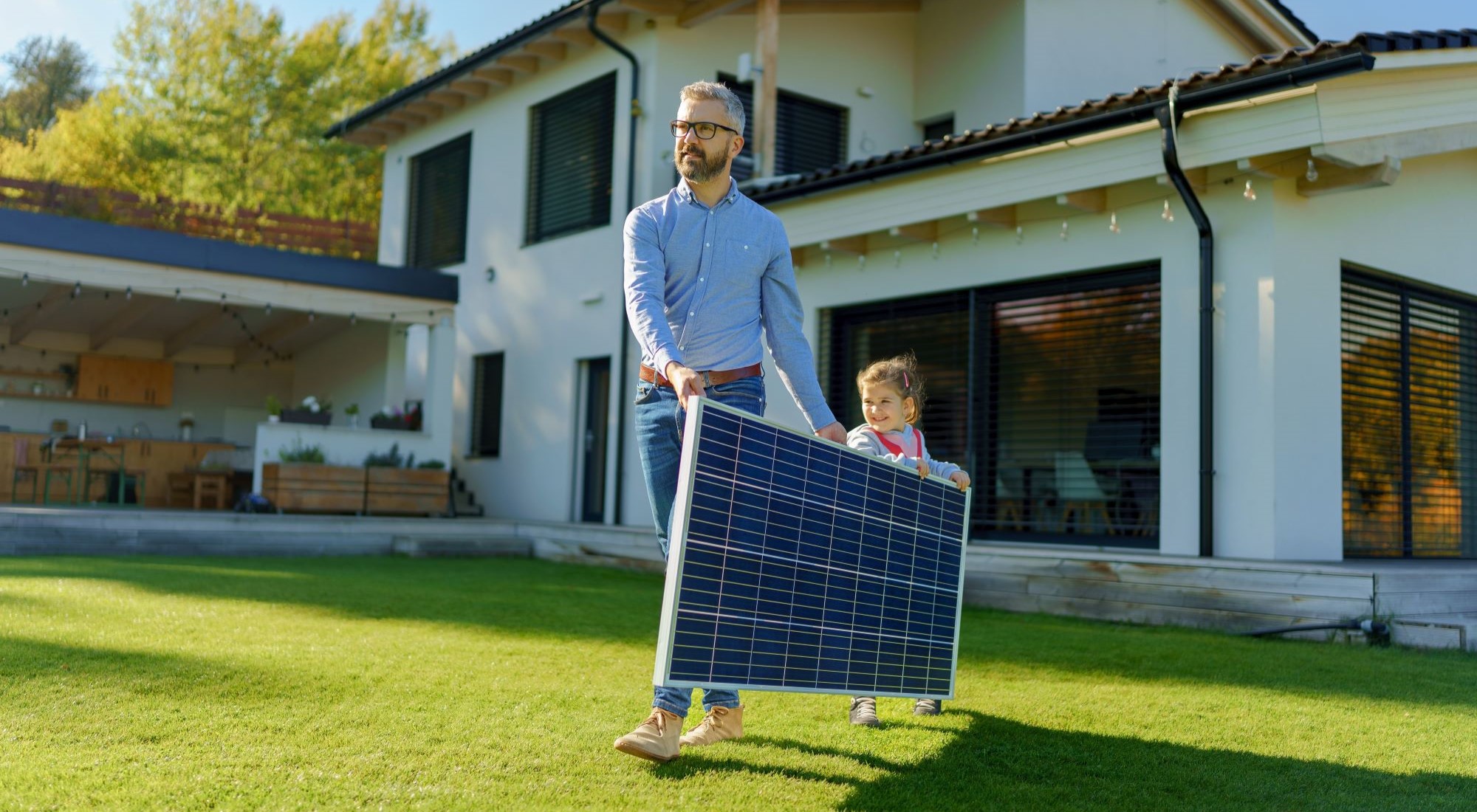 ein Vater und seine Tochter tragen ein PV-Panel durch den Garten