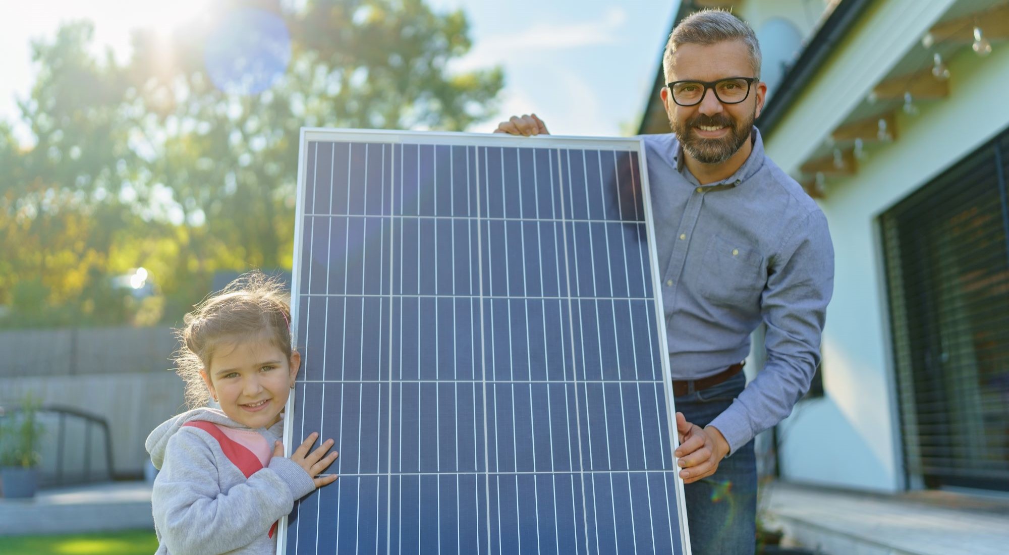 ein Vater und seine Tochter halten von Nahem ein PV-Panel in die Kamera